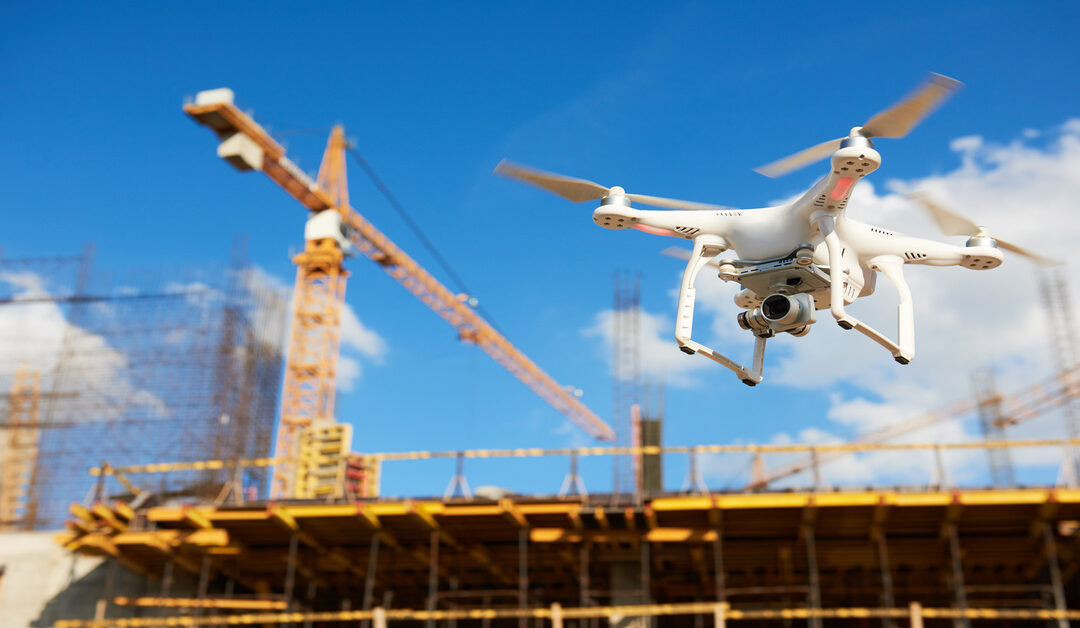 A drone flies above an active construction site with tower cranes and steel framework under a clear blue sky.