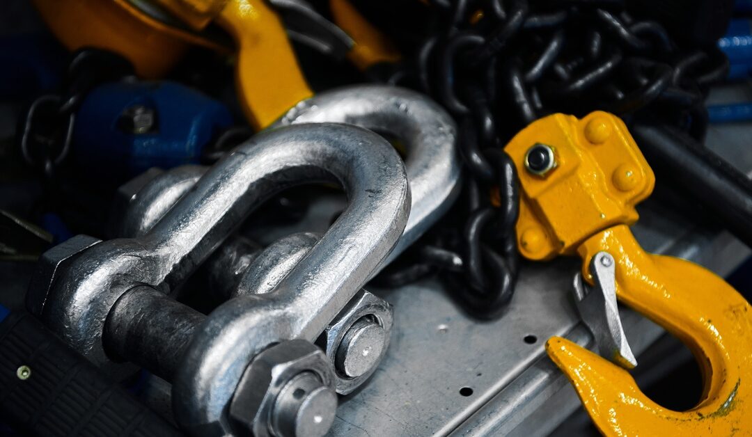 A large metal shackle and a yellow lift hook lays next to heavy chains on industrial rigging equipment.